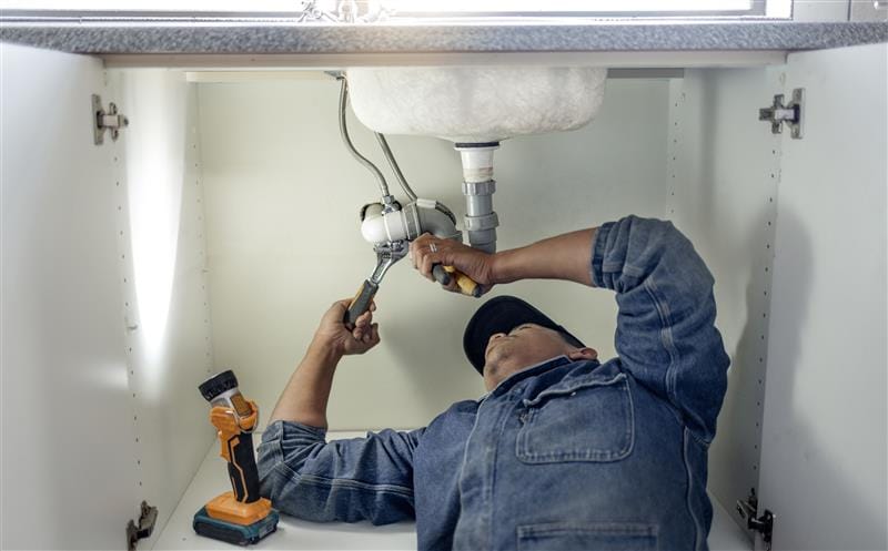 Plumber repairing pipes beneath a bathroom sink in Santa Cruz