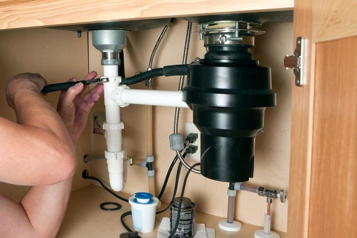 Plumber installing a garbage disposal beneath a kitchen sink in Santa Cruz