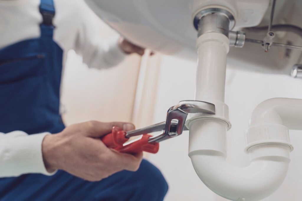 Plumber repairing a white drain pipe beneath a sink in Santa Cruz