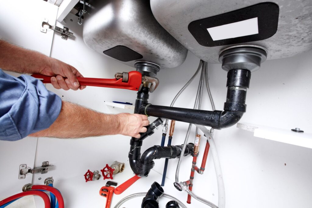 Plumber repairing drain pipes beneath a kitchen sink in Santa Cruz
